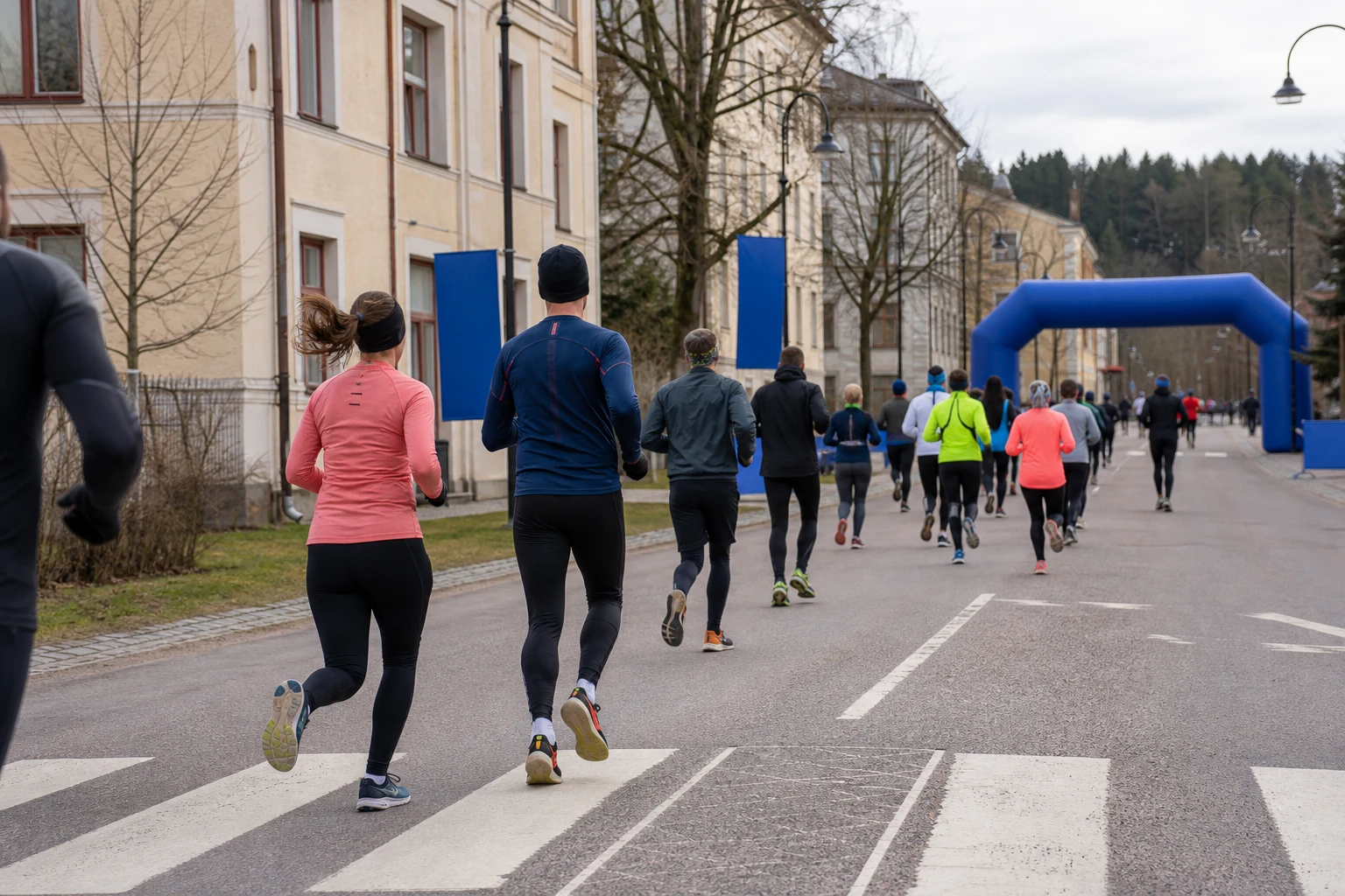 Löpare i klunga längs en gata med publik bakom staket